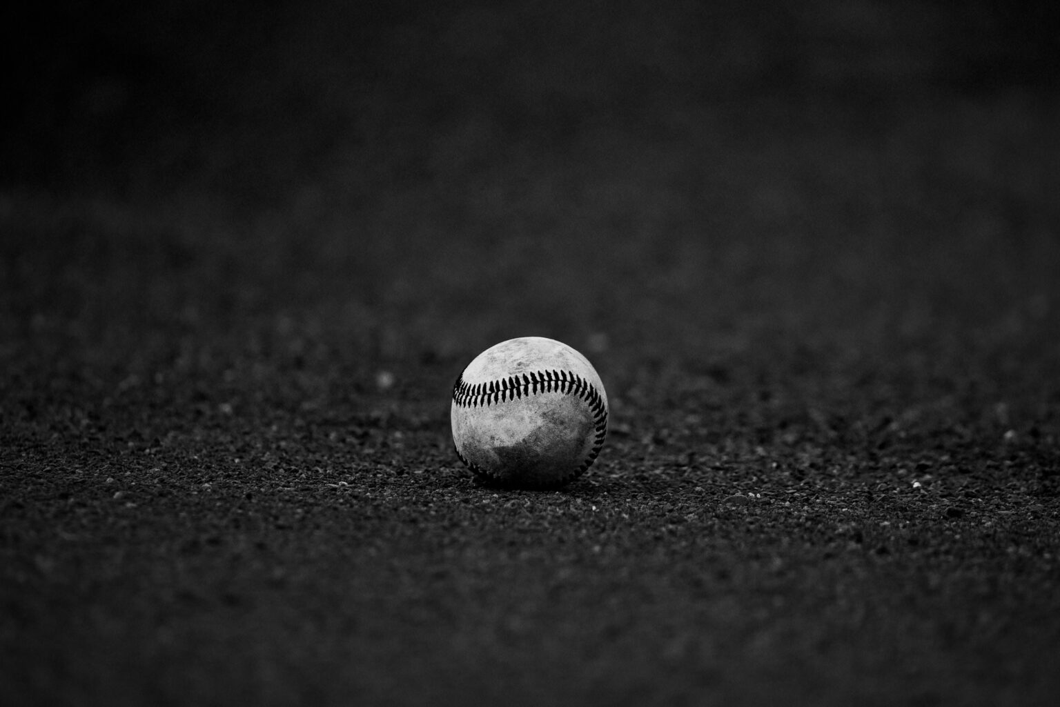A monochrome image of a baseball resting on a textured dark surface, perfect for sports themes.